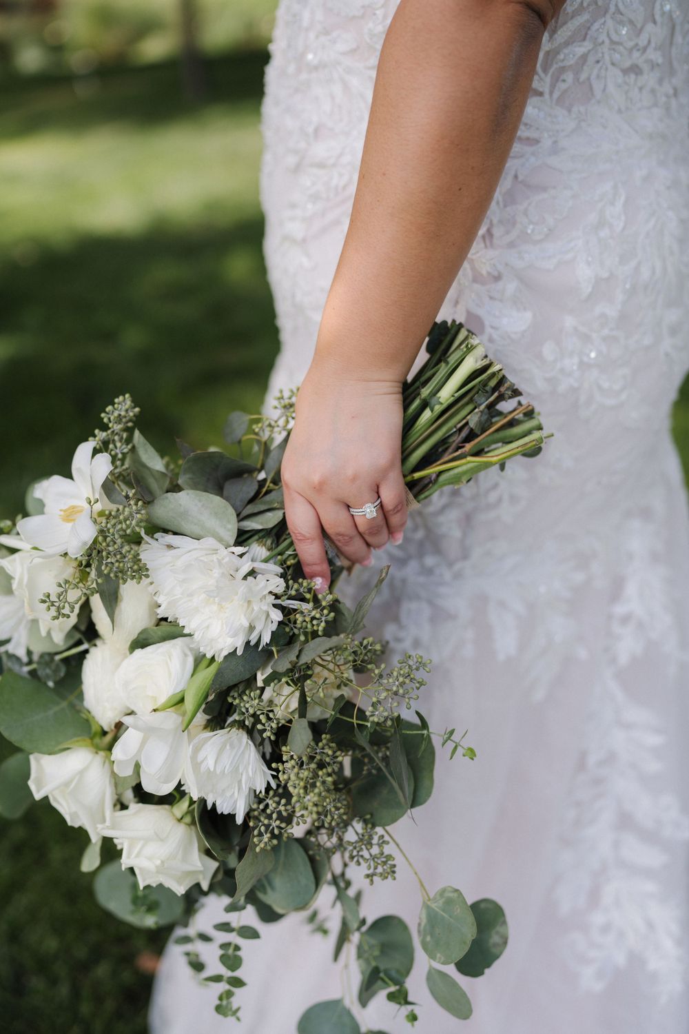Close-up of bride holding elegant white floral bouquet with eucalyptus leaves against lace wedding dress.