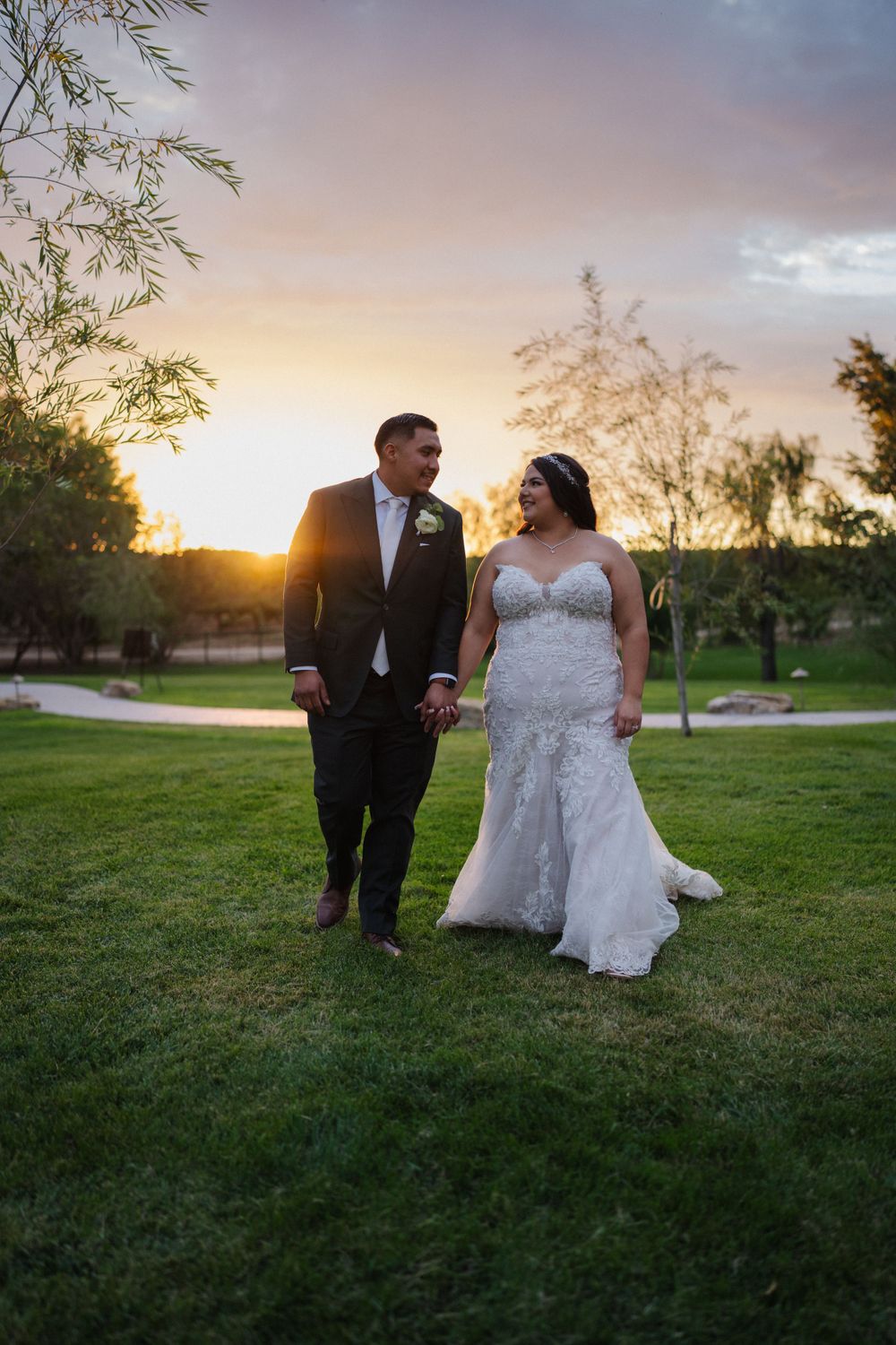 Newlyweds walking on grass during golden hour sunset at outdoor wedding venue.
