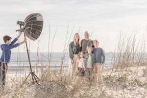 Behind-the-scenes photo of beach family portrait session with lighting equipment visible.