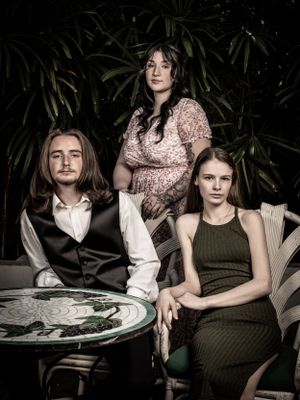 Moody vintage-style portrait of three people seated at a table with tropical plants in background. Family portrait photography.