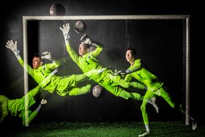 Soccer goalkeepers in neon yellow uniforms diving dramatically to save a ball against dark background in multiple exposure shot.