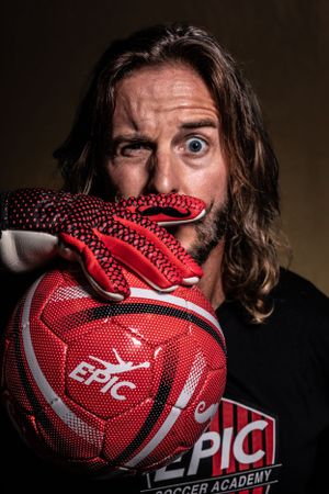 Person in black shirt with a red EPIC soccer ball in dramatic lighting. Portrait photography.