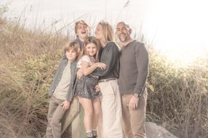 Family group portrait in casual attire against golden sunset in tall grass.
