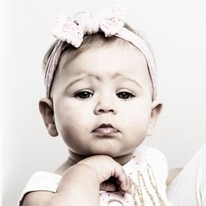 Black and white portrait of a baby wearing a pink floral headband against light background.