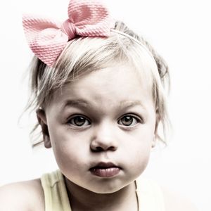 A small figure with blonde hair wearing a tank top and pink bow headband poses against white background.