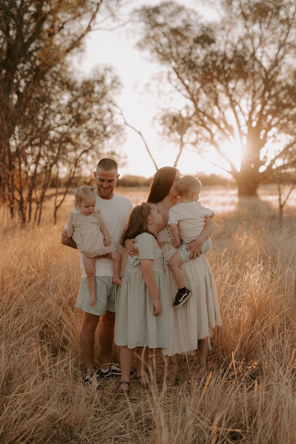 Family wearing white outfits poses together in a golden field at sunset.