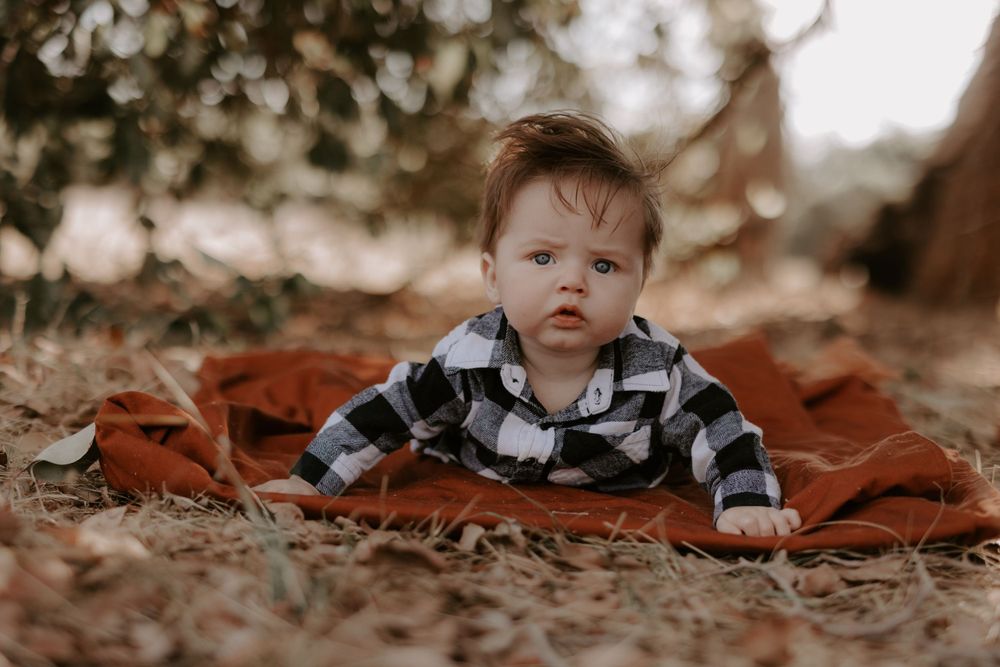 Baby in plaid outfit rests on rustic blanket during fall outdoor photoshoot.