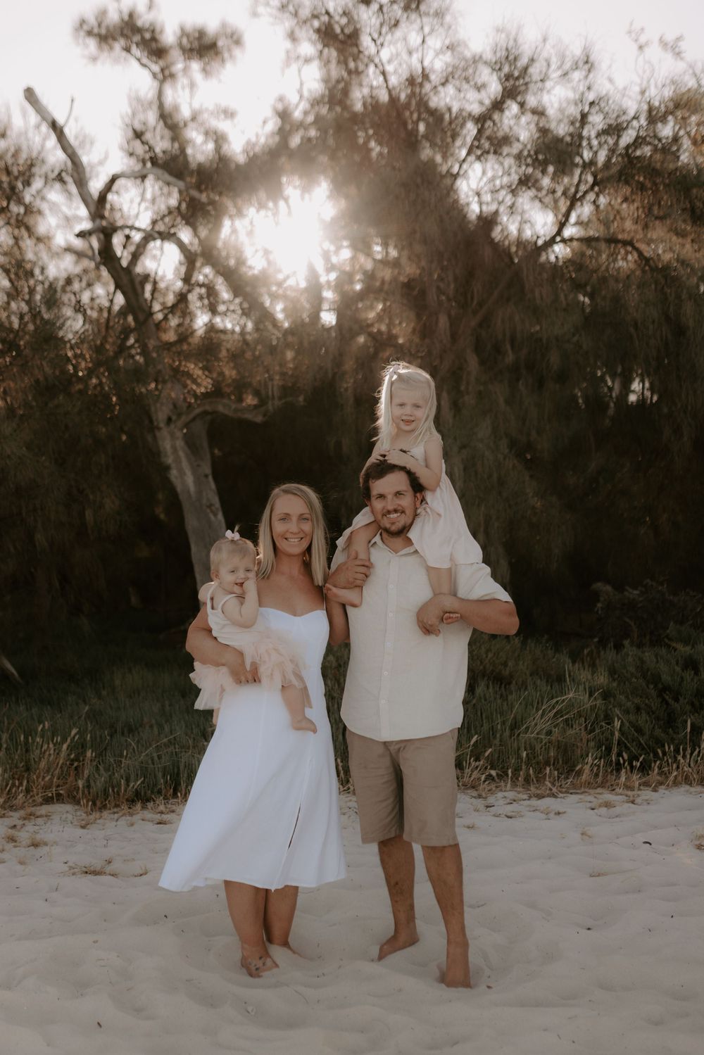 Family in white and beige outfits playing together on sandy beach at dusk.