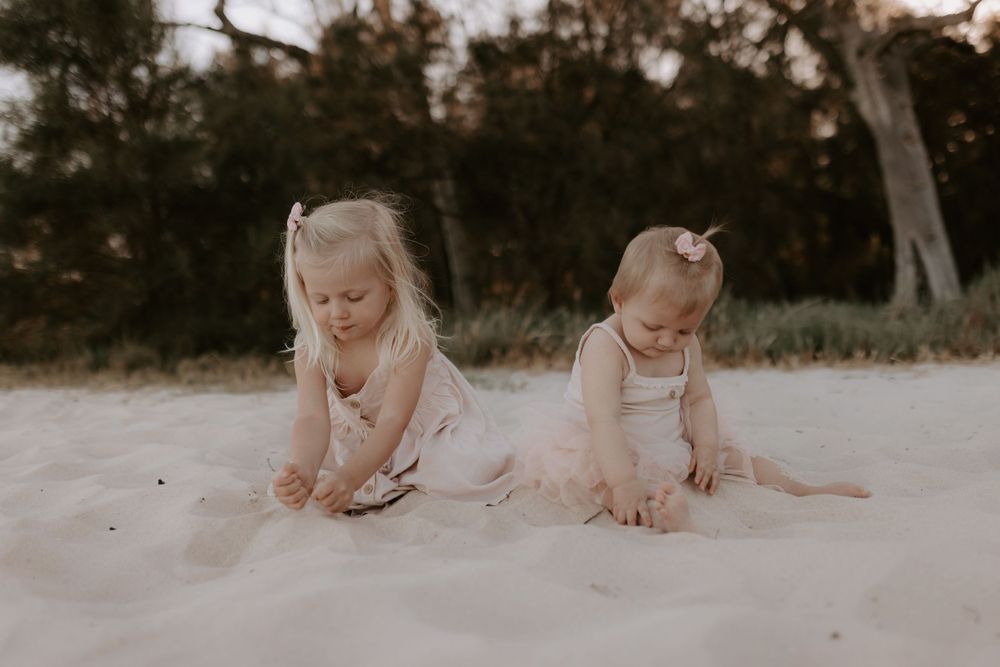 Children playing and crawling on sandy beach during sunset photoshoot.