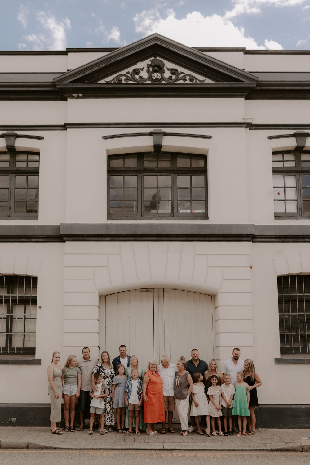 Large group photo of people lined up against white industrial building exterior.