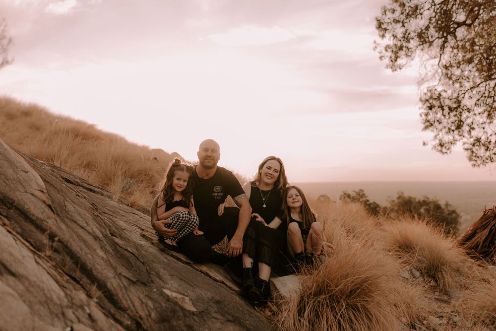 Family relaxing together on a hillside during sunset photoshoot.