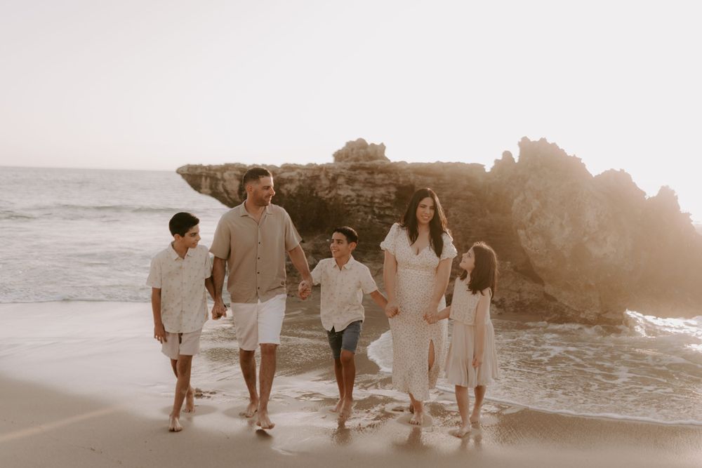 Family walking together along a scenic beach at sunset with rocky cliffs in the background.
