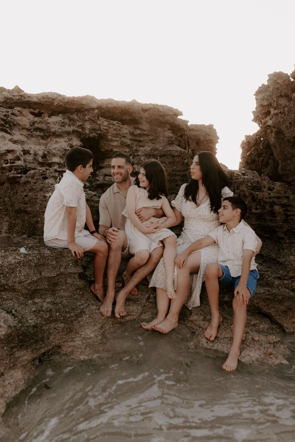 Family sitting together on rocky beach formation during sunset photography session.