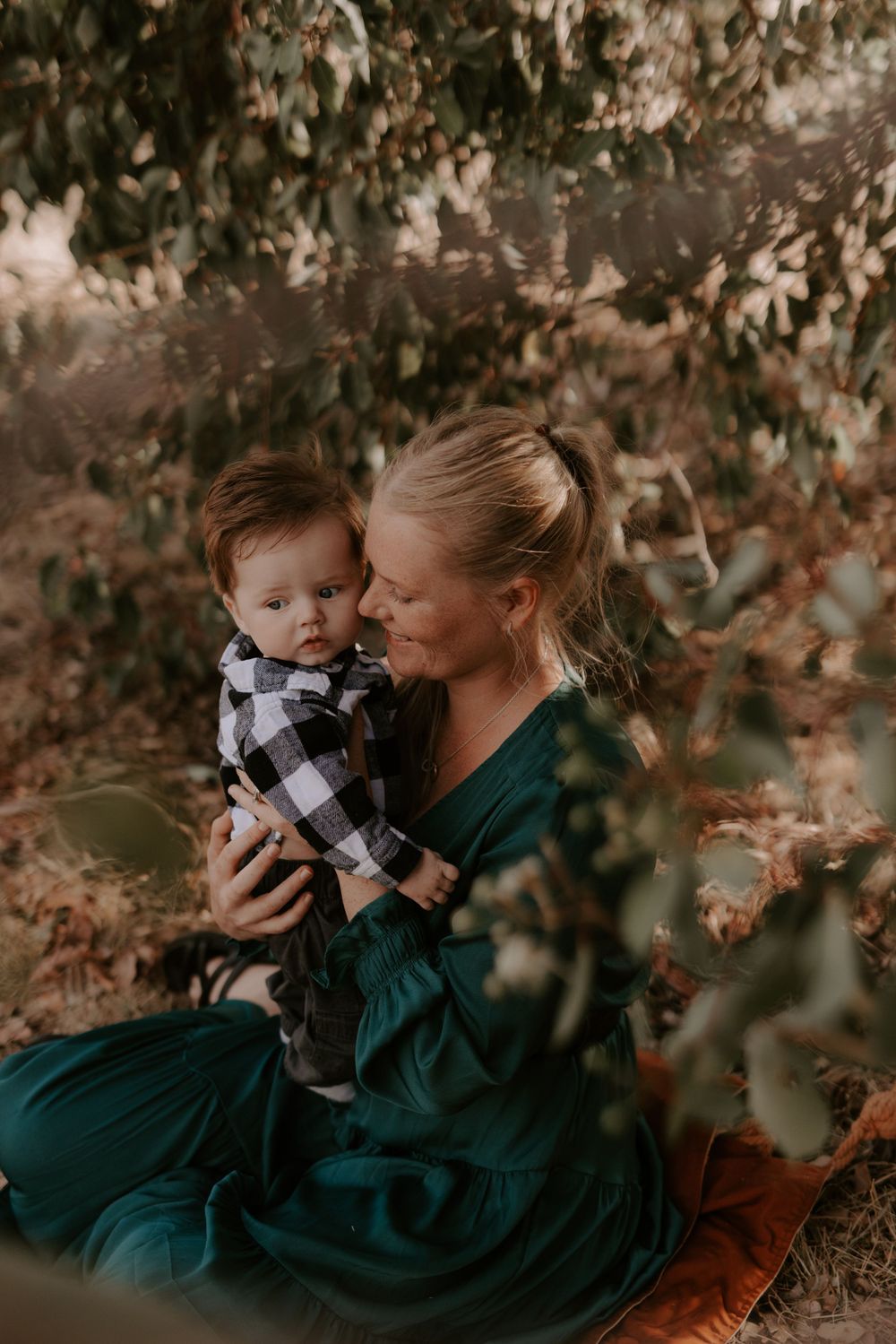 Mother and baby share sweet moments among autumn foliage in green dress.