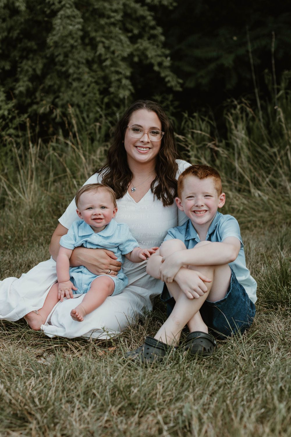 A family portrait taken outdoors with natural lighting and tall grass in the background.