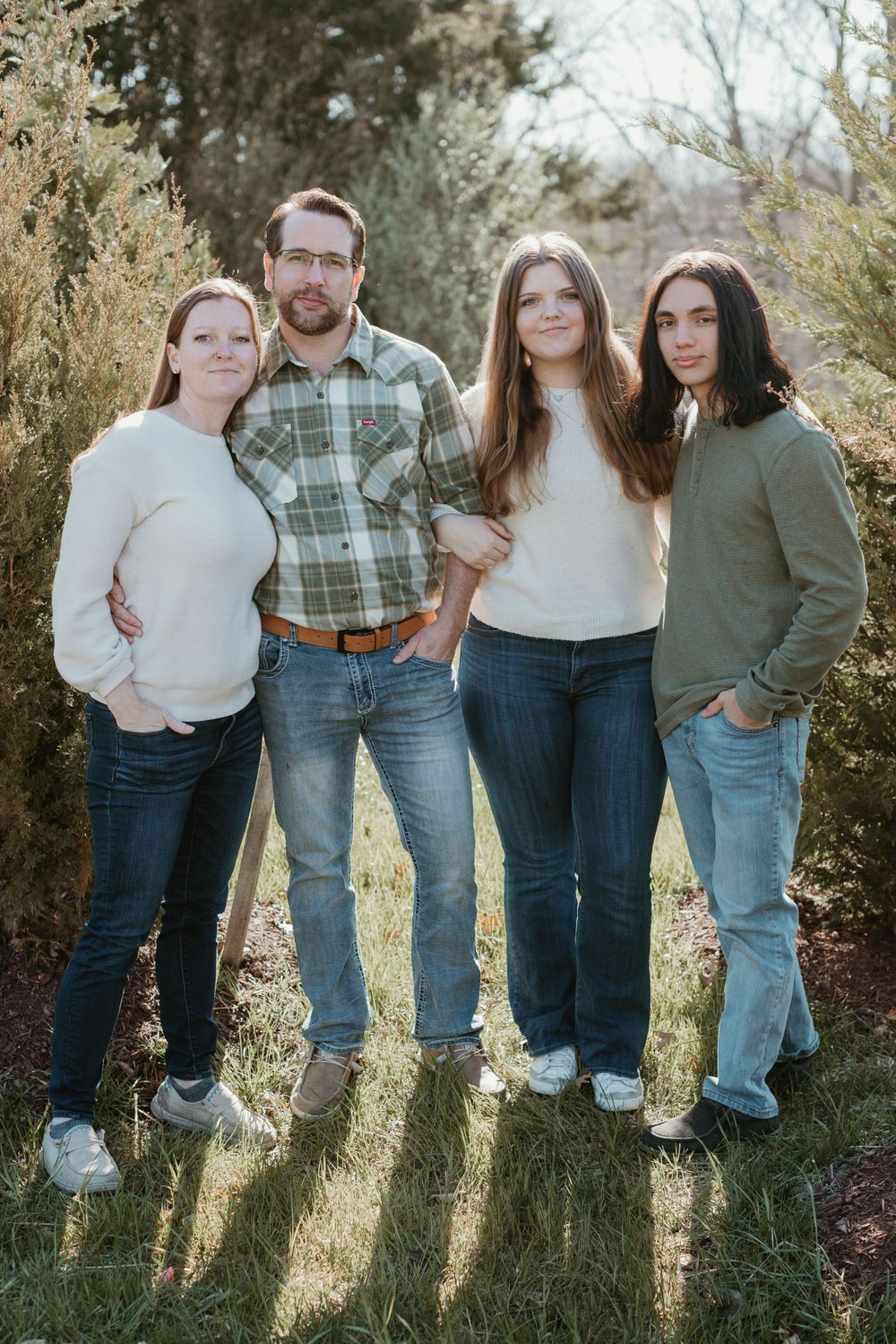 Family wearing coordinated casual outfits poses together in outdoor setting with natural lighting.