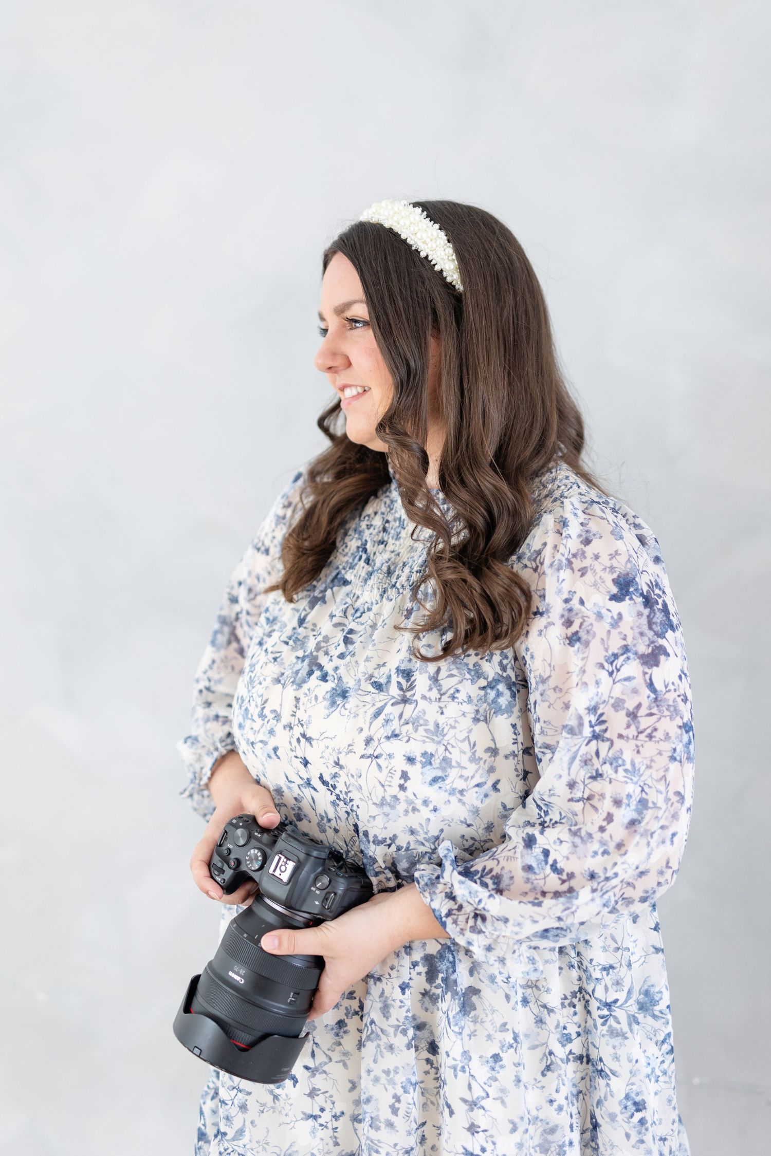 Female wedding photographer in floral dress holding Canon camera, laughing to the side.