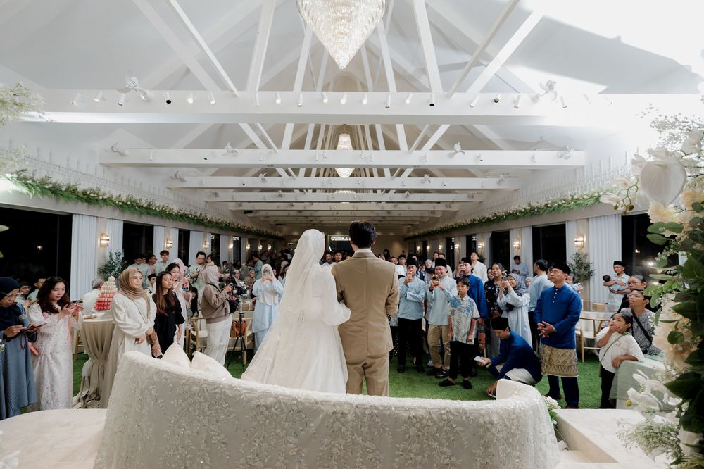 Elegant outdoor wedding ceremony with bride and groom at the altar surrounded by guests under a white pergola with floral decor.