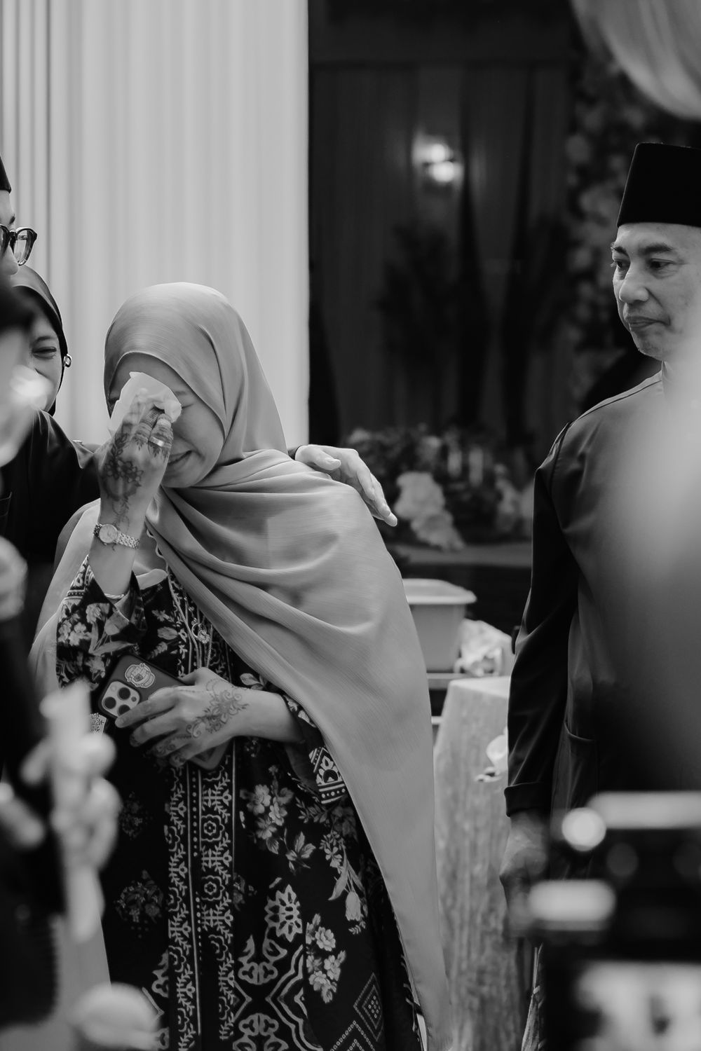 Black and white photo of emotional woman in hijab being comforted at a formal Malay cultural ceremony.