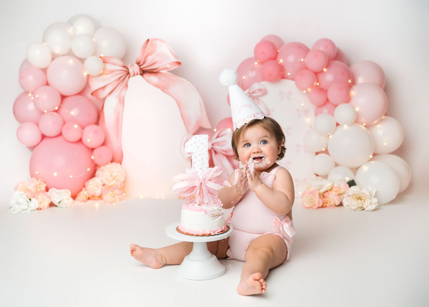 Baby girl enjoying a pink and white balloon cake smash during a first birthday photography session in Linden, New Jersey.