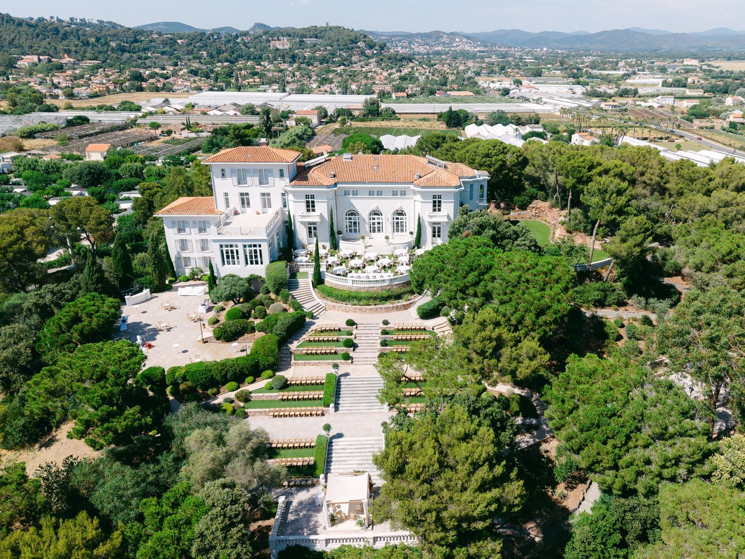Aerial view of a luxurious French Riviera villa with manicured gardens, terracotta roof, and lush surrounding landscape.