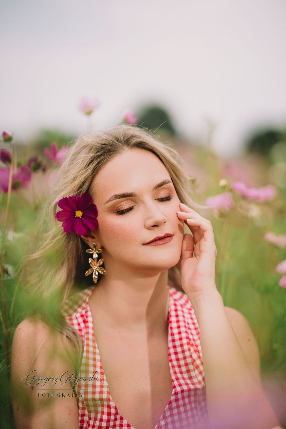 Blonde woman with flower in hair posing eyes closed in pink cosmos flower field.
