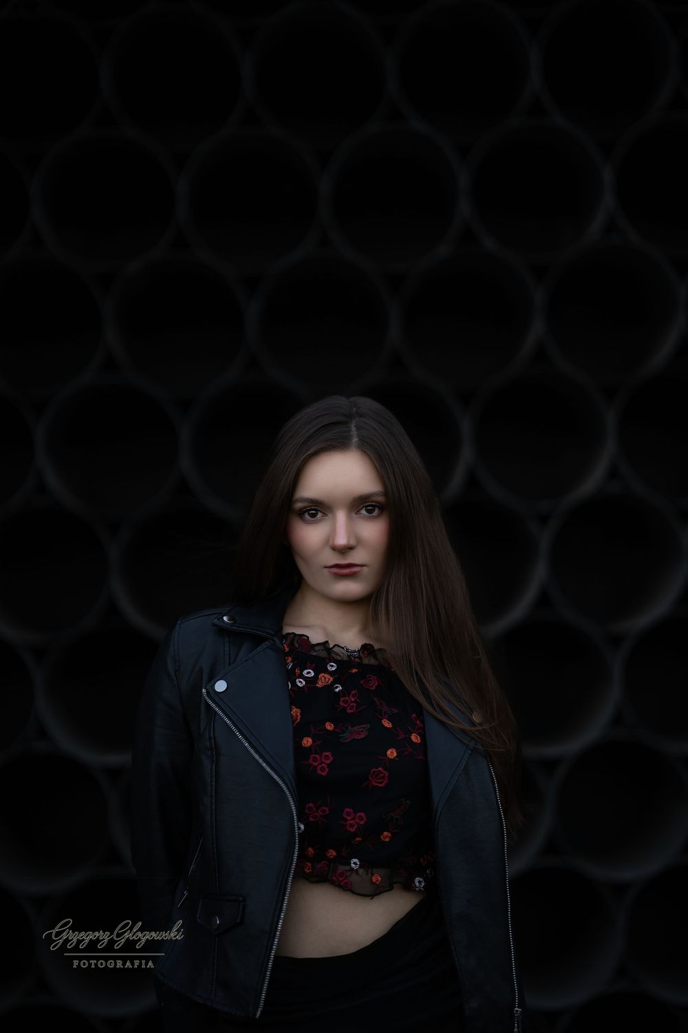 Young woman in leather jacket poses against dark circular tube wall background.