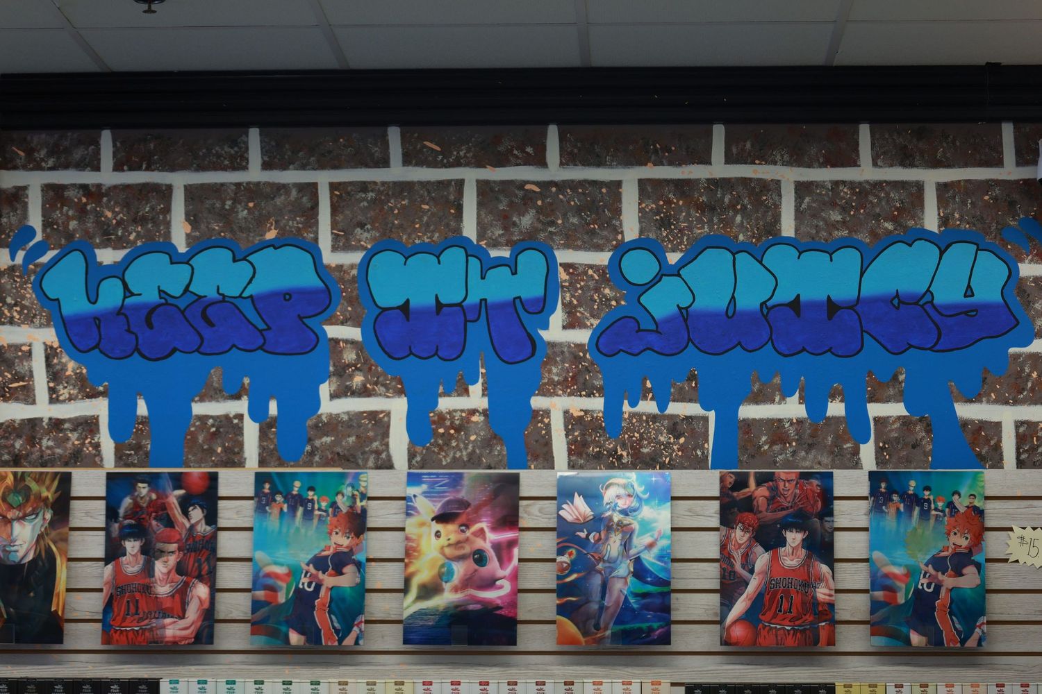 Colorful graffiti art in blue bubble letters displayed above anime artwork prints on a slatwall in a retail store.