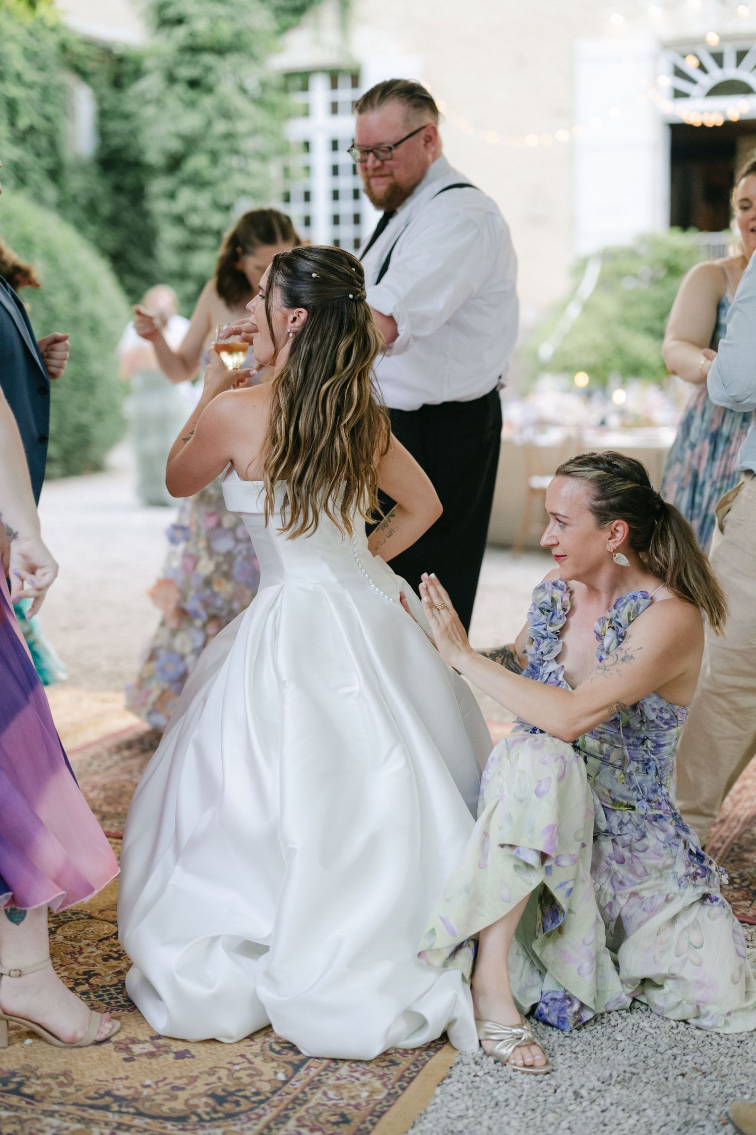 Bride in white gown dancing joyfully with guest in floral dress at outdoor wedding reception.