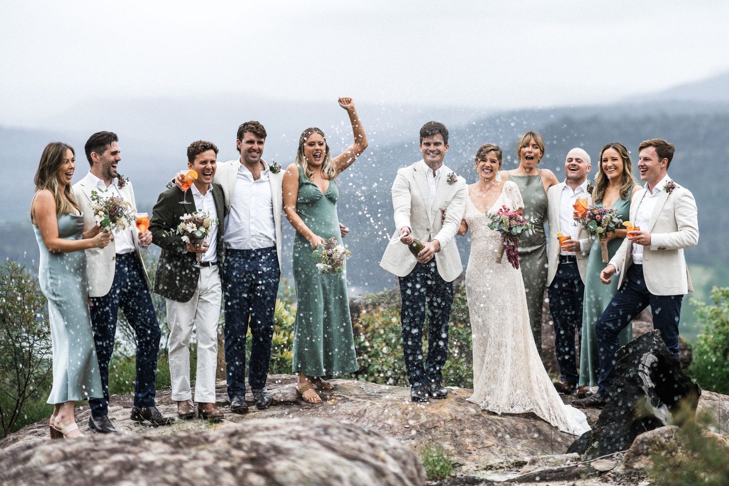 The bridal party celebrates with a champagne spray at Kangaroo Valley Bush Retreat’s rocky lookout, with sweeping views of Kangaroo Valley.