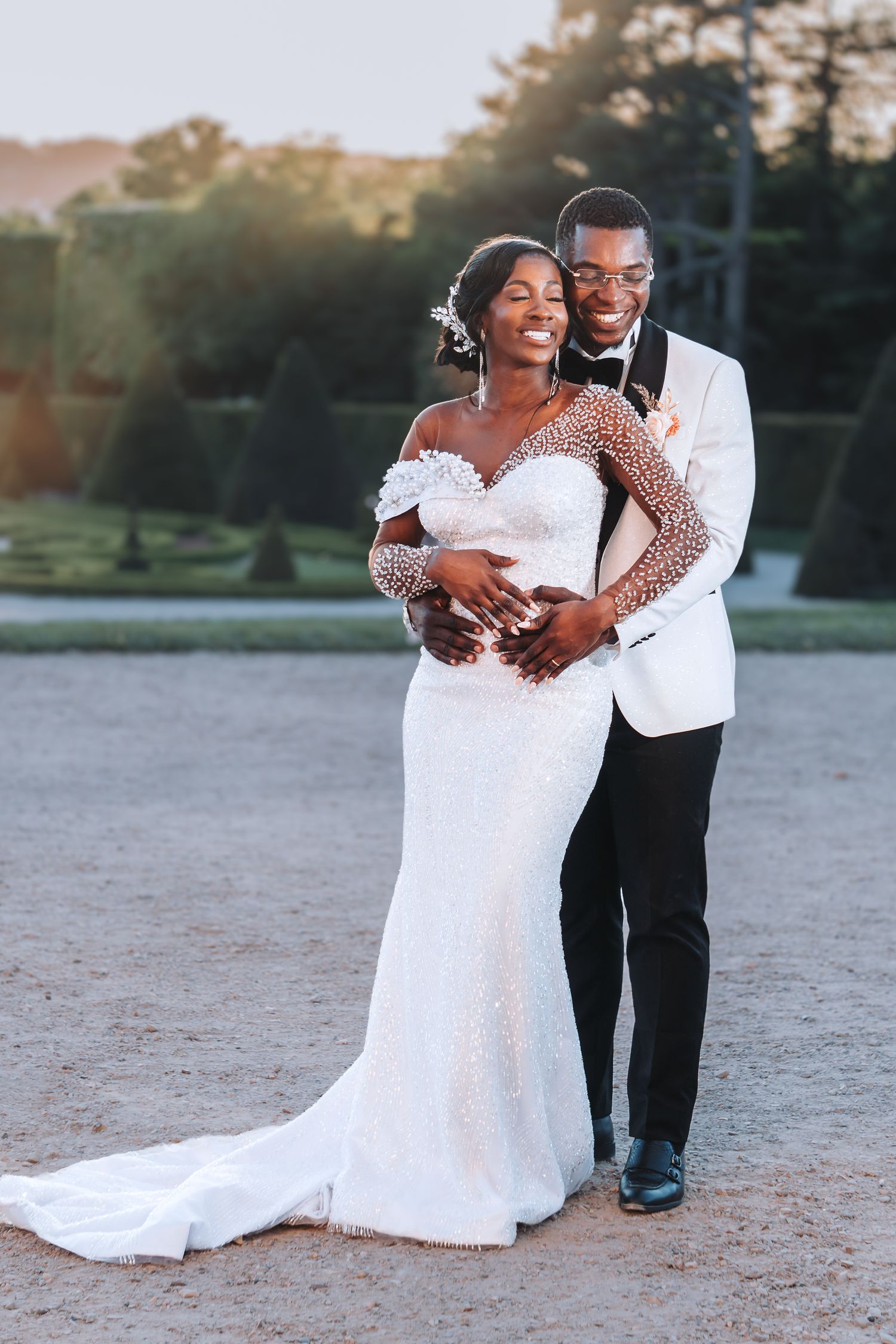 Elegant bride and groom embracing at golden hour in a formal French garden setting.