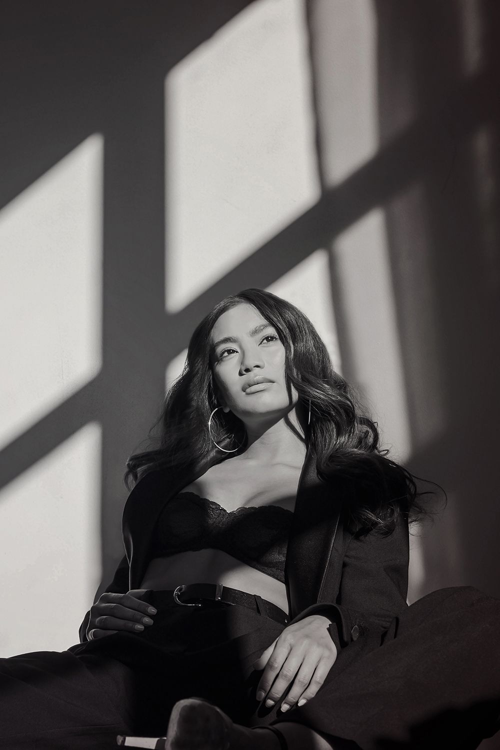 Dramatic black and white portrait with window light casting geometric shadows and creating moody contrast on subject.