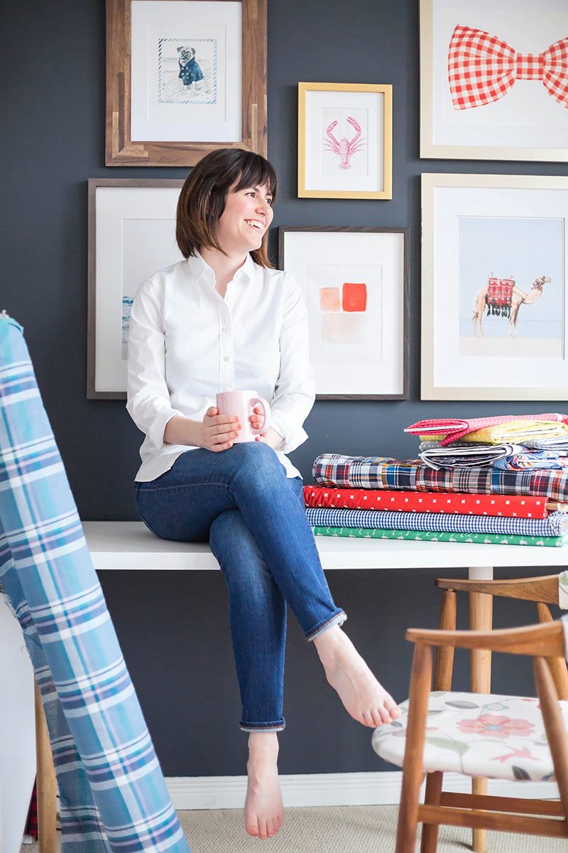 Person sitting on a desk against a dark wall with gallery wall of whimsical framed artwork.
