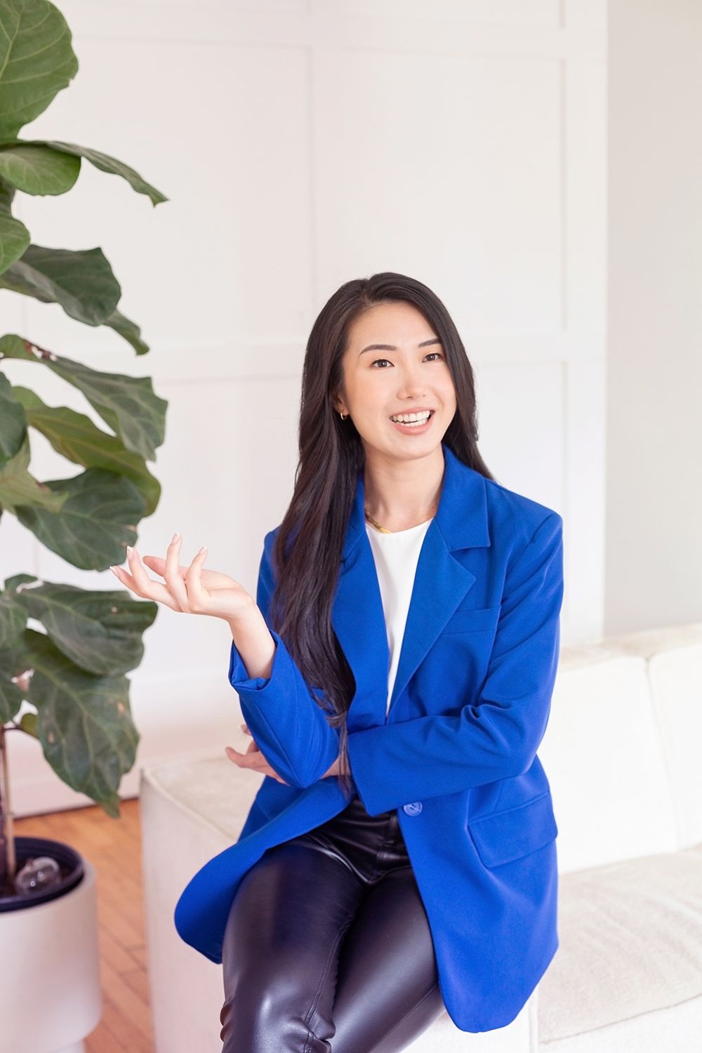 Professional in vibrant blue blazer seated casually next to indoor plant.