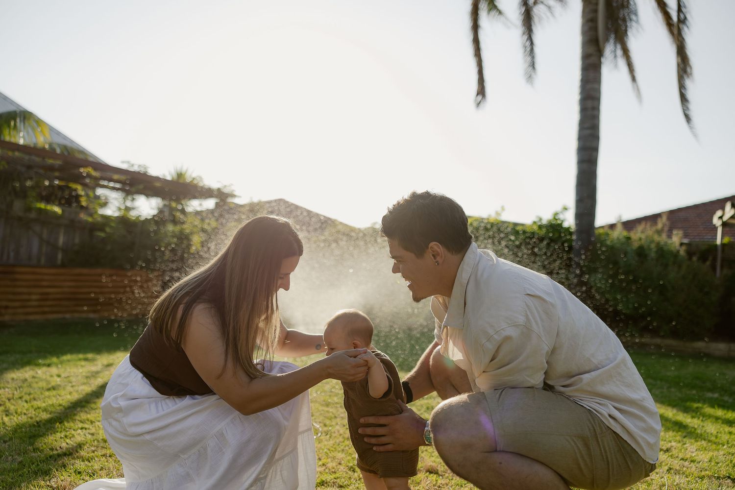 Parents support their baby standing outdoors during a warm, natural in-home lifestyle photoshoot in Mandurah.