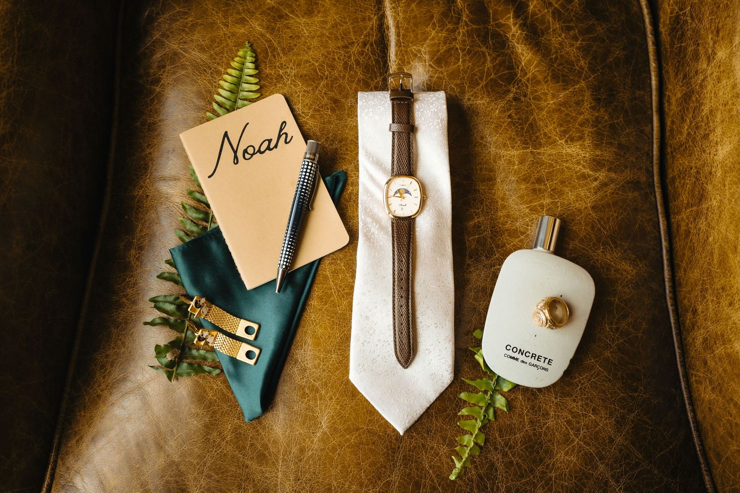 Groom wedding details flat lay with Noah notebook, watch, tie, cologne, and boutonniere.
