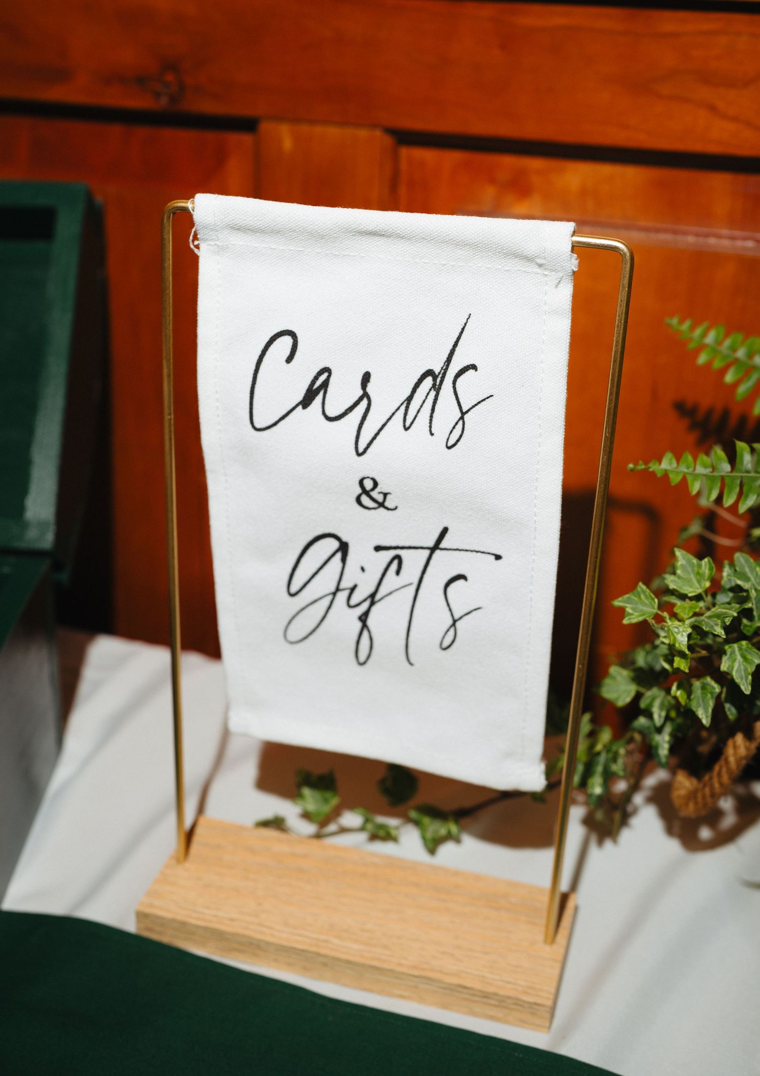 Elegant gold and wood Cards & Gifts sign with calligraphy script displayed on a green table at a wedding reception.
