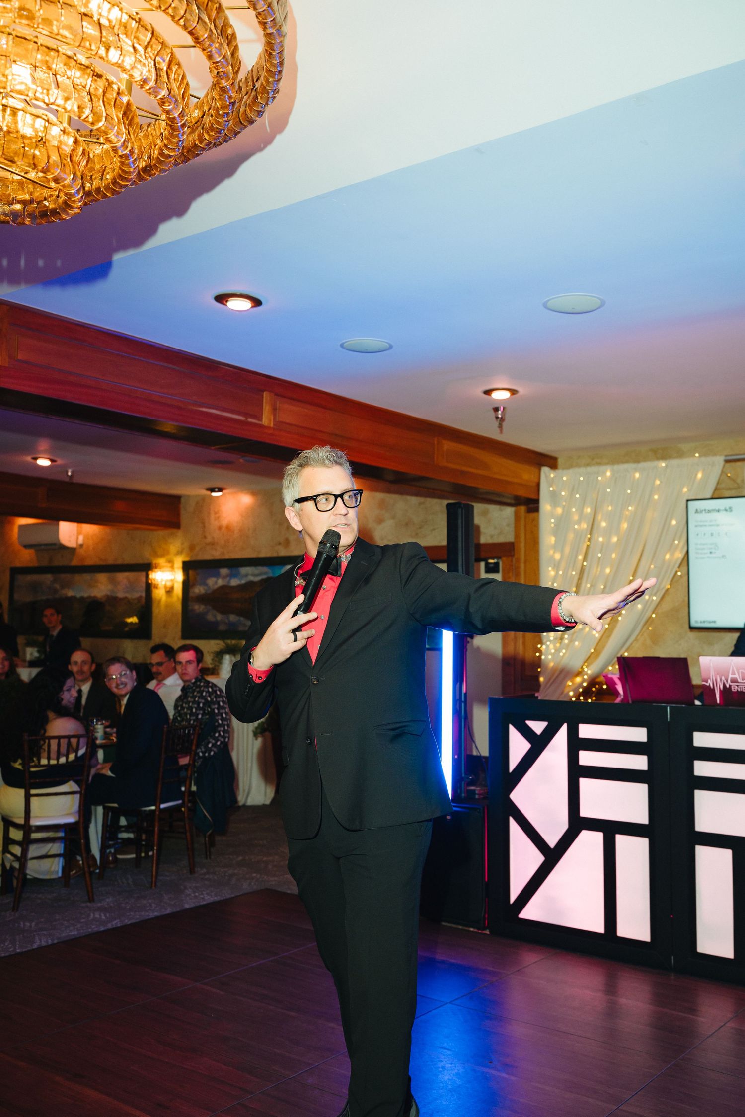 A charismatic emcee in a black suit and red tie performs with a microphone at an elegant wedding reception venue.