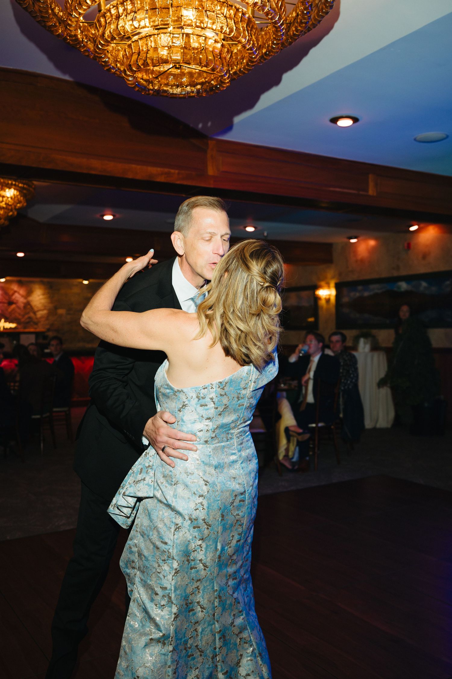 Couple shares an elegant first dance under a golden chandelier at a formal wedding reception.