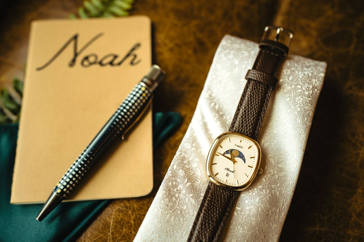 Close-up of grooms wedding accessories including Noah journal, elegant watch, and silk tie.