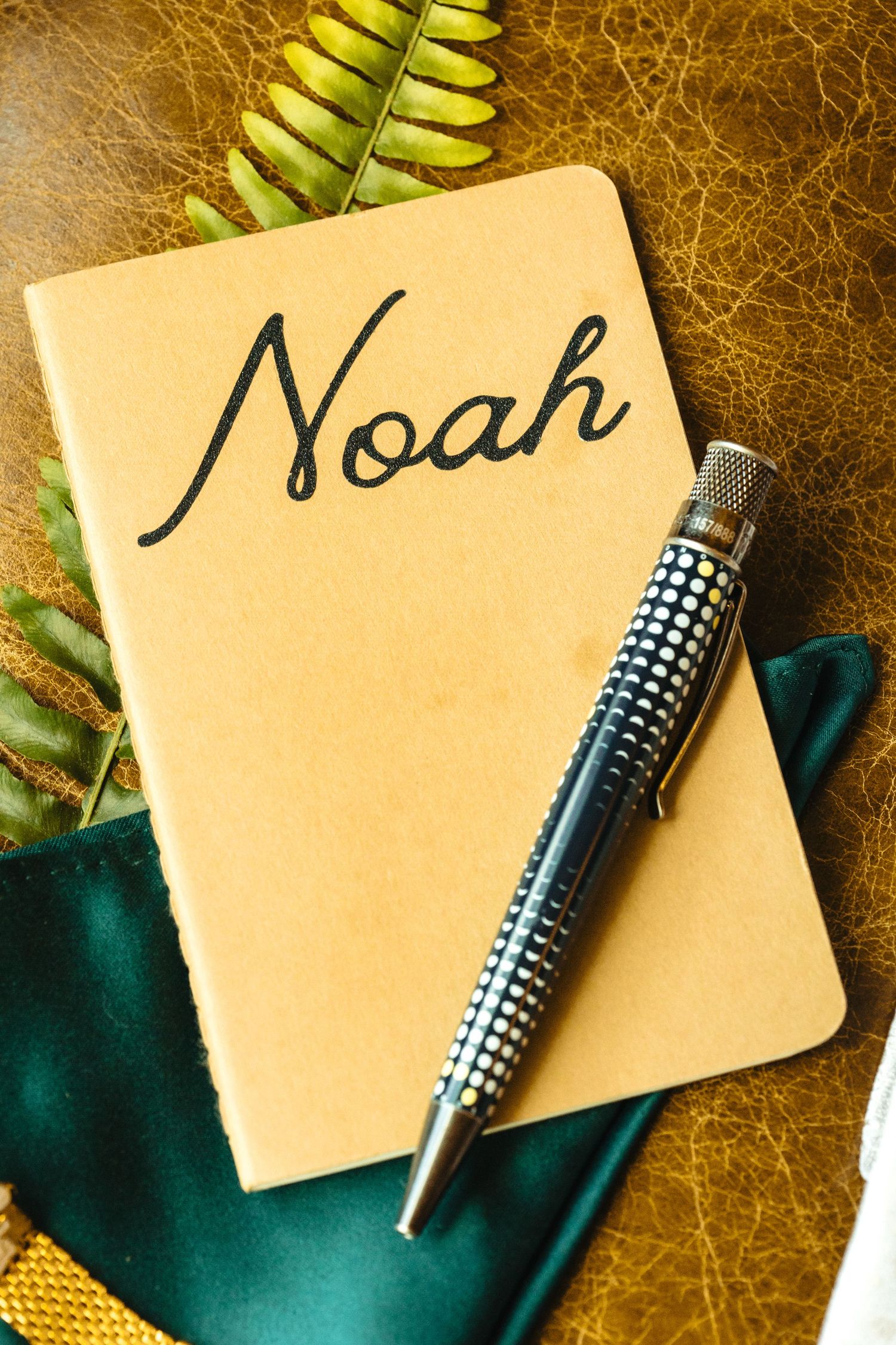 Personalized kraft paper notebook with Noah written in script, topped with a decorative pen on leather.