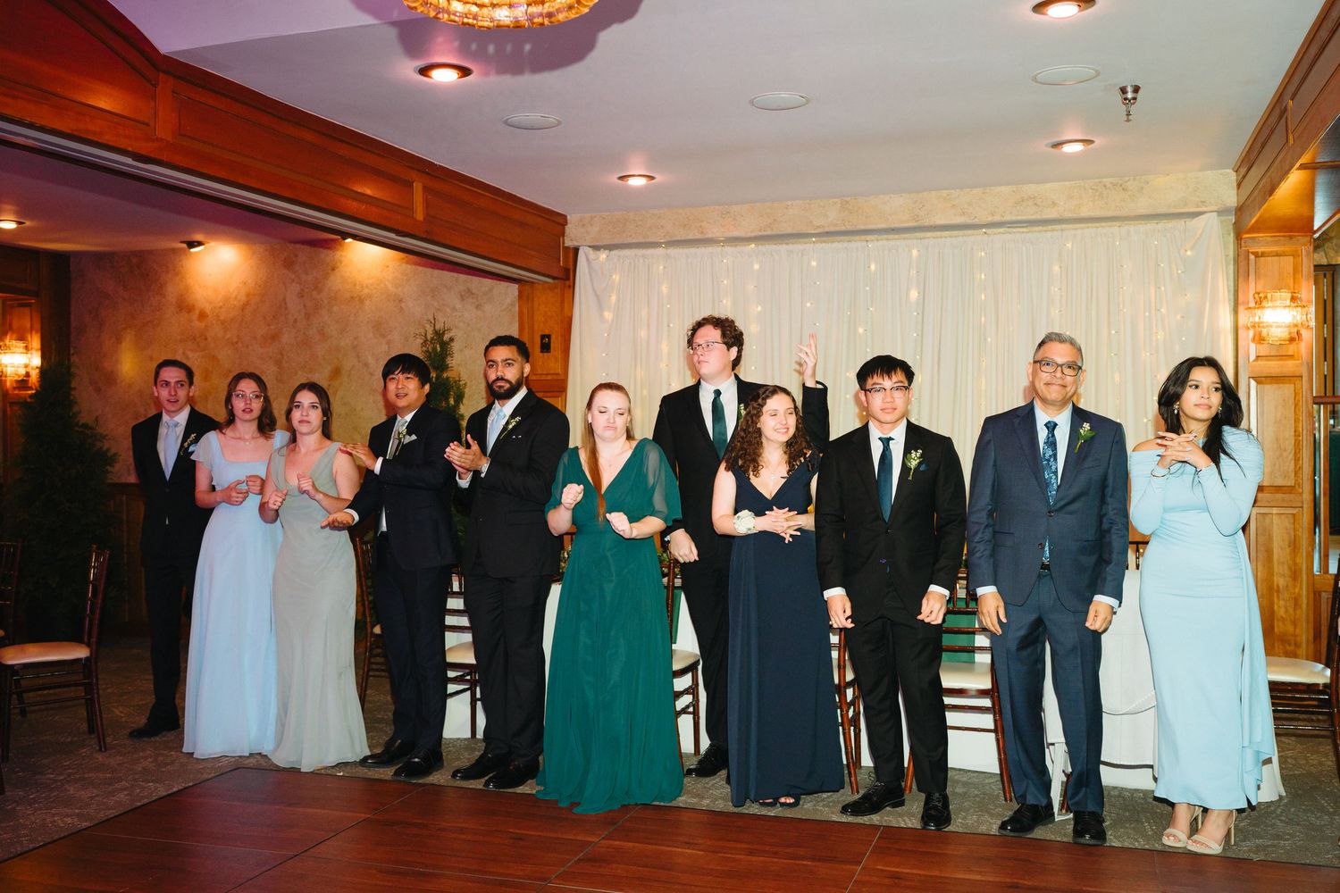 Wedding party lineup in formal attire with green and blue gowns at reception.
