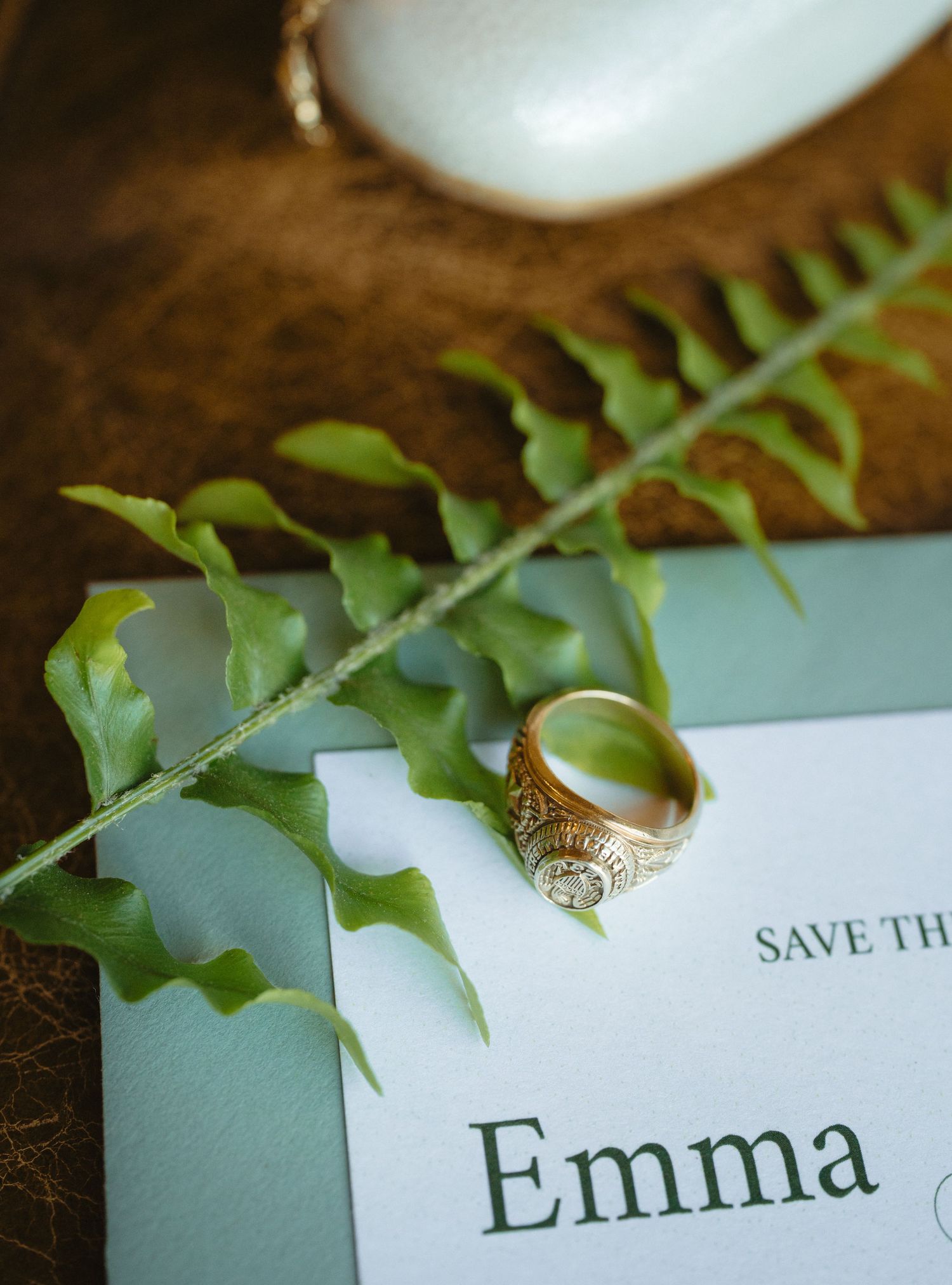 Gold vintage wedding ring resting on a fern leaf beside an elegant Save the Date card for Emma.