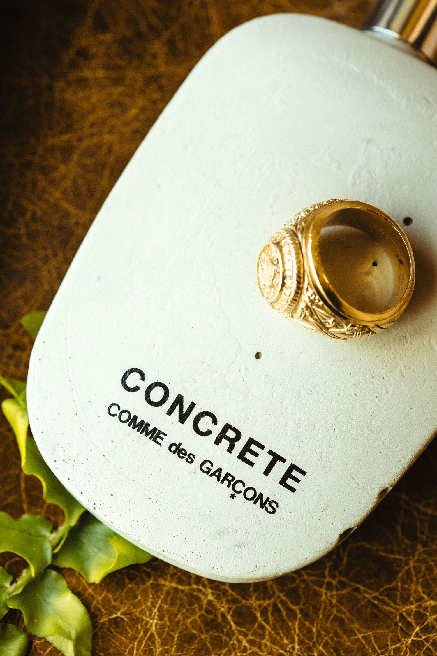 Gold signet ring resting on a Concrete Comme des Garcons perfume bottle on a leather surface.