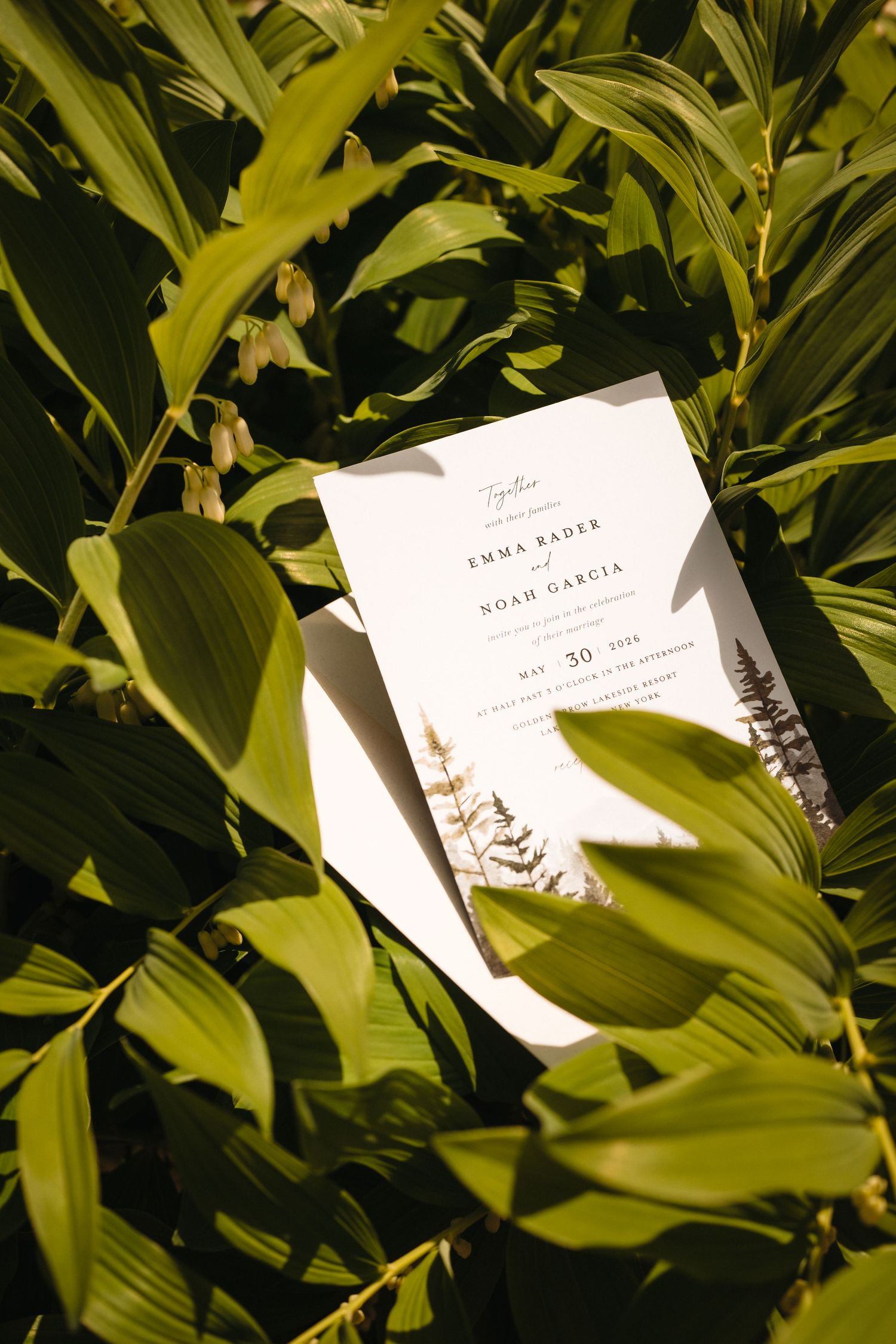 Elegant wedding invitation for Emma Bader and Noah Garcia nestled among lush green tropical leaves.
