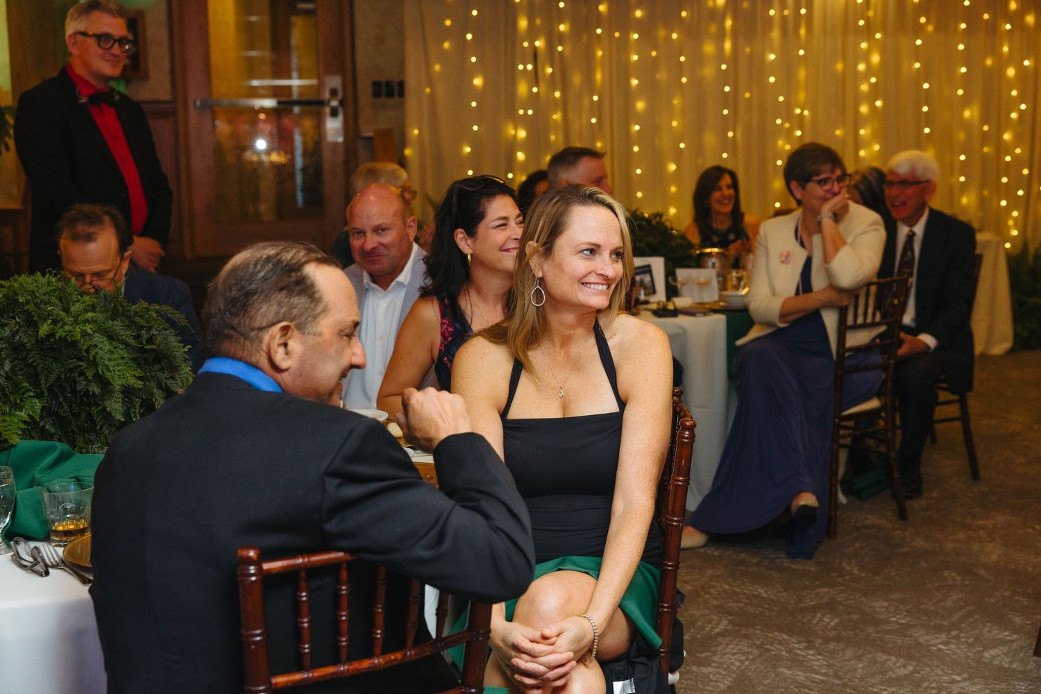 Guests socializing at elegant wedding reception with warm string light backdrop.