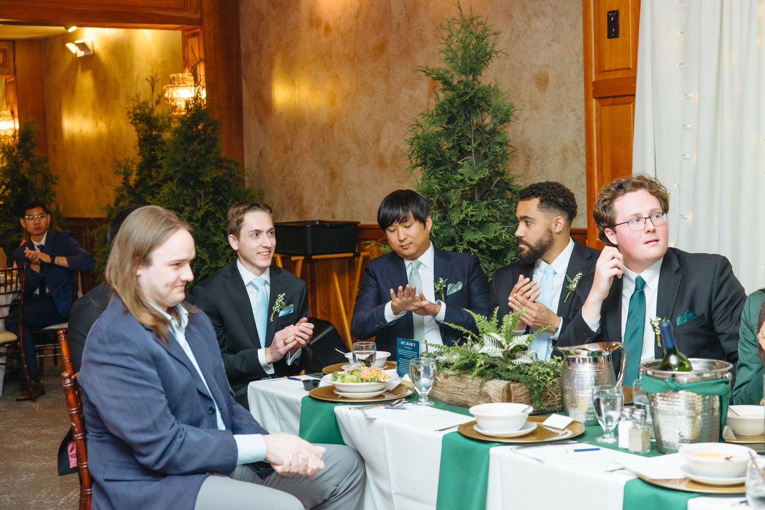 Five men in formal attire enjoy conversation at a elegantly decorated wedding reception dinner table.