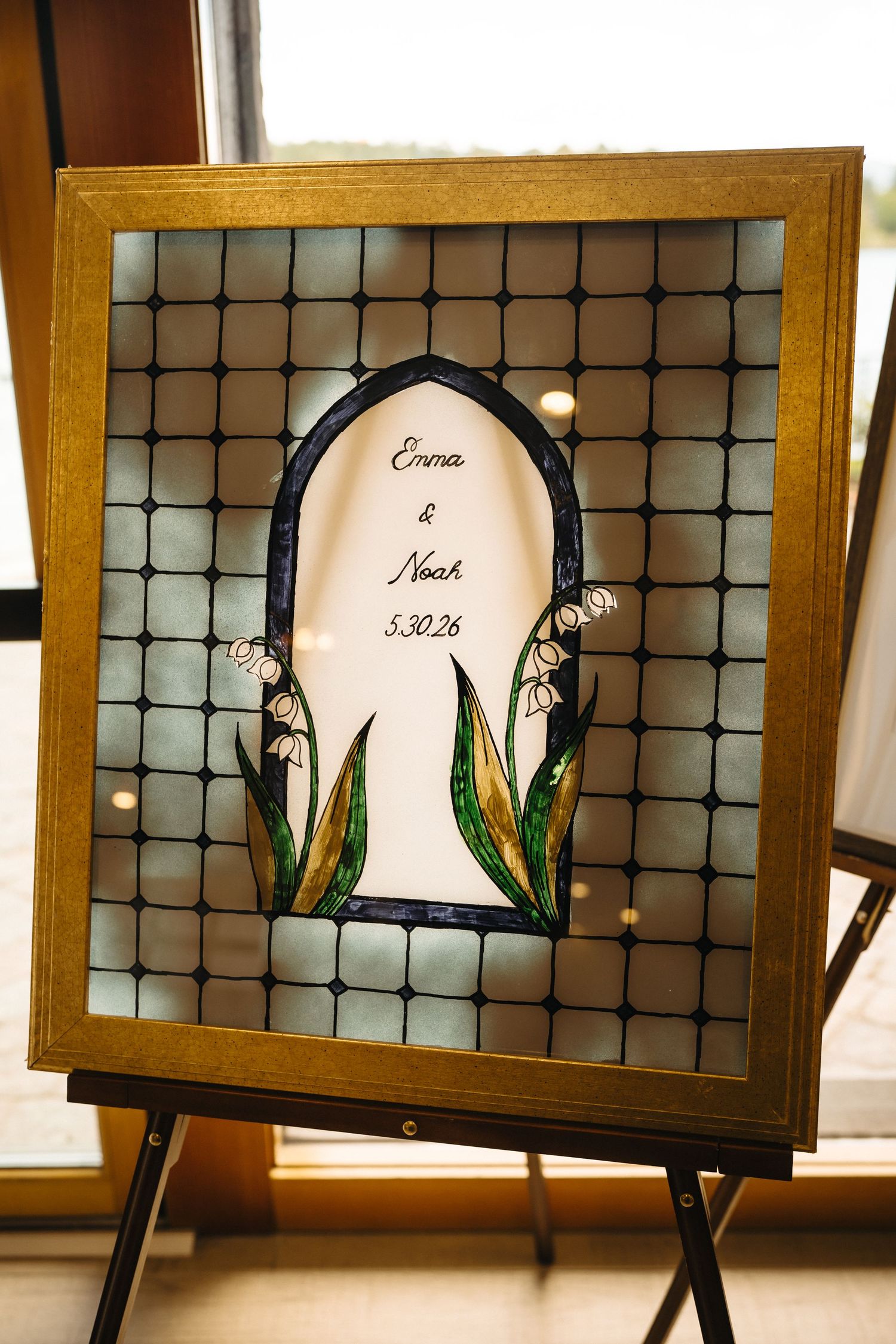 Stained glass wedding sign reading Emma and Noah 5.30.26 with lily of the valley design on easel.