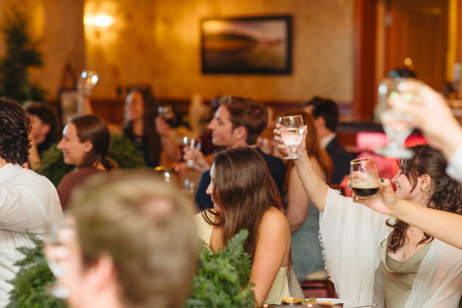 Wedding guests raising glasses in a toast during a reception dinner at an elegant restaurant.