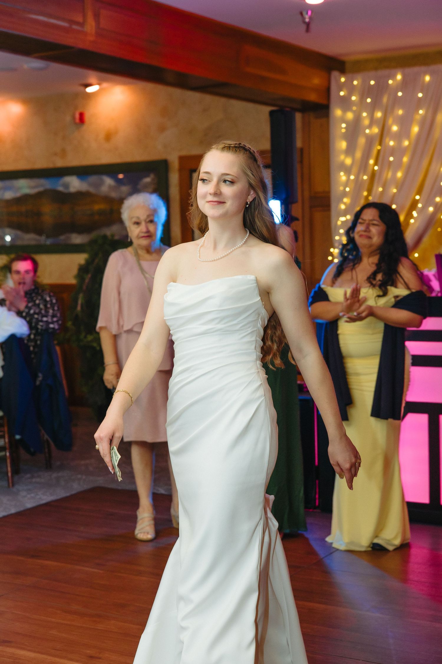 Smiling bride in strapless white mermaid gown walks across wedding reception dance floor.